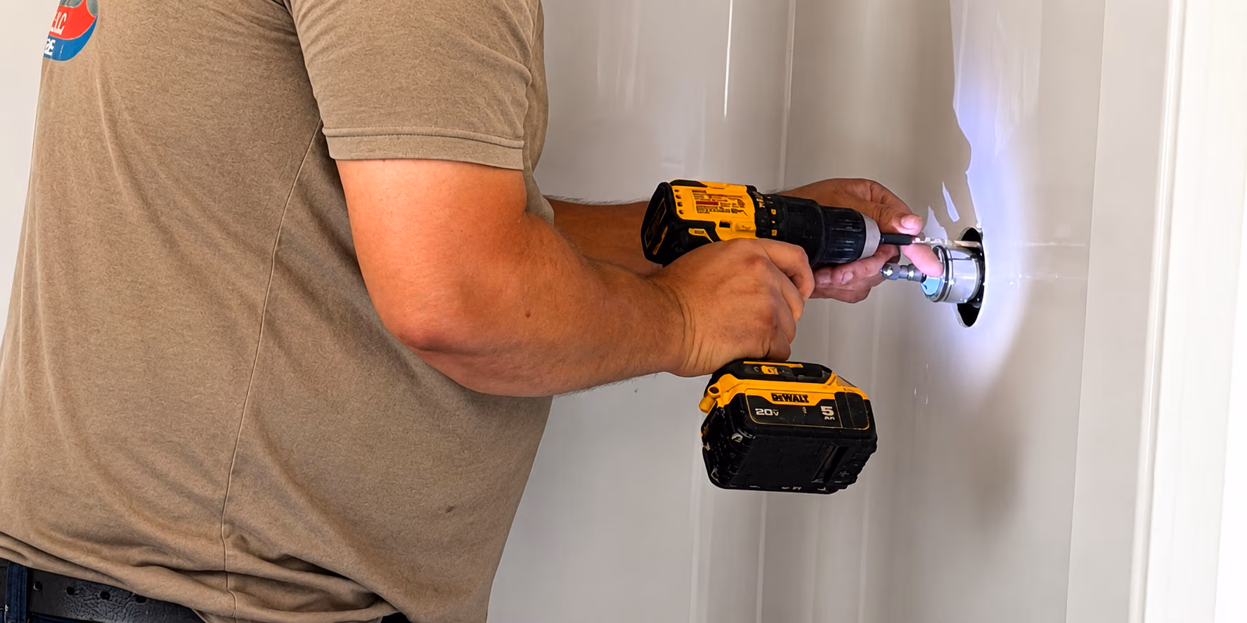 A person using a yellow cordless drill to install or repair a fixture on a white wall.